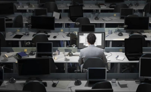 A single person working at a desk in an otherwise empty office of cubicles